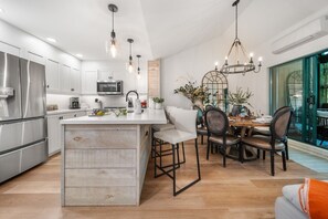 A modern kitchen with stainless steel appliances, a central island, and a dining area with a chandelier. - Near Gondola & Lake | Private Hot Tub| Free Ski Shuttle & Parking (Whistler)