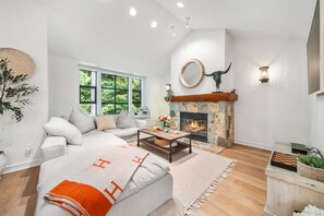 A modern living room with a stone fireplace, a sofa, a coffee table, and a large window. - Near Gondola & Lake | Private Hot Tub| Free Ski Shuttle & Parking (Whistler)