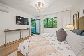 Ein Schlafzimmer mit einem Bett, einem Fernseher, einem Fenster und einer Tür zu einem Außenbereich.
