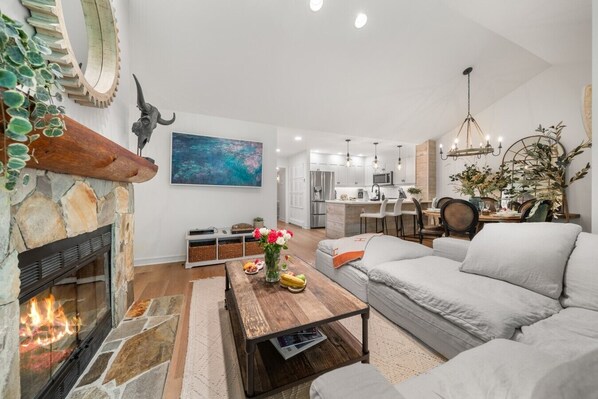 A modern living room with a stone fireplace, a dining area, and a kitchen in the background. - Near Gondola & Lake | Private Hot Tub| Free Ski Shuttle & Parking (Whistler)