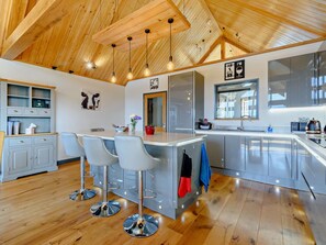 A modern kitchen with a central island, bar stools, and a wooden ceiling.