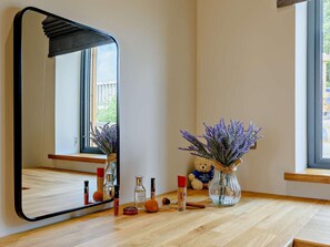 A bathroom with a large mirror, a wooden vanity, a teddy bear, and a vase with lavender.