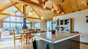 Une cuisine spacieuse dotée d’un grand îlot central, de poutres en bois et de luminaires suspendus.