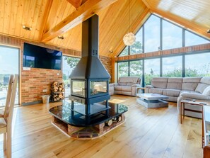 Un salon moderne doté d’un poêle à bois, d’une cheminée en briques et d’une grande fenêtre donnant sur un jardin.