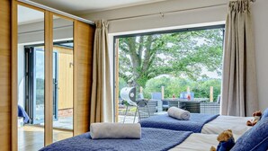 Une chambre avec deux lits, une porte-fenêtre coulissante donnant sur un espace extérieur et une vue sur la verdure.