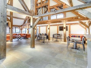 Ett rymligt interiört utrymme med synliga träbjälkar, stengolv och en blandning av olika sittgrupper, inklusive soffor och bord.