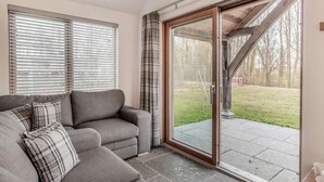 Una habitación con sofá gris, cojines escoceses, puerta corredera de vidrio a un espacio exterior y estructura de techo de madera.