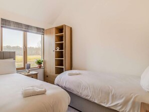 Un dormitorio con dos camas, un armario de madera, una mesita de noche con lámpara y una ventana con vistas al exterior.