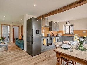 A modern kitchen with a stainless steel refrigerator, built-in oven, and washing machine. There is a dining area with a wooden table and chairs. - 2 Bed in Norwich (oc-91298) (Corpusty)