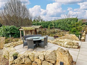 An outdoor patio with a round table and chairs, surrounded by stone walls and greenery.