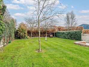 Ein gepflegter Garten mit Rasenfläche, Baum und Hecke.