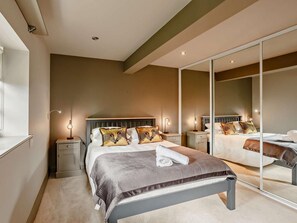 A modern bedroom with a large mirror, a bed with patterned pillows, bedside lamps, and a bench.