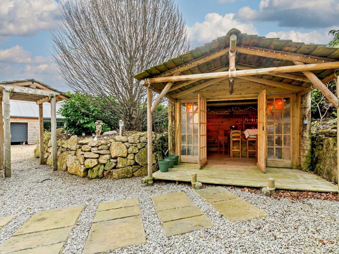 Eine rustikale Holzhütte mit Steinwand, einer Holzveranda und einem Steinpfad zum Eingang.