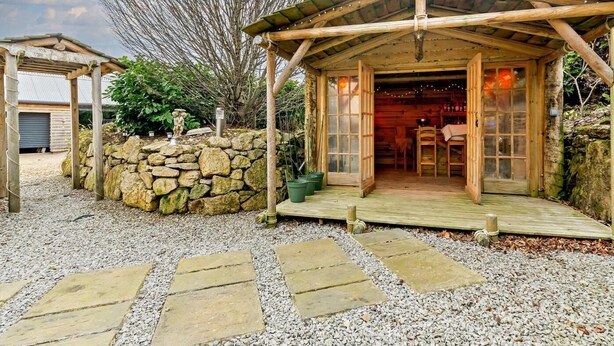 Eine rustikale Holzhütte mit Steinwand, einer Holzveranda und einem Steinpfad zum Eingang.