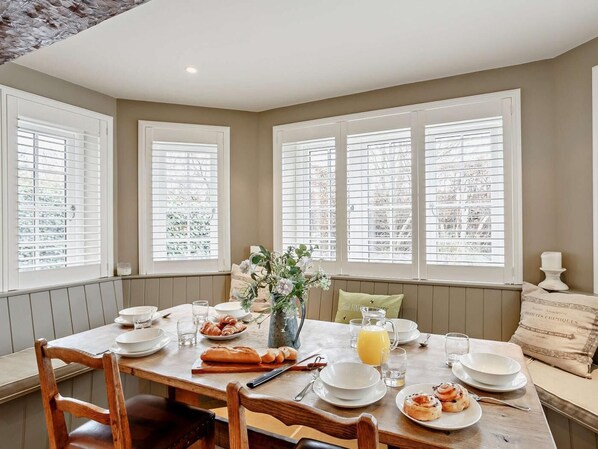 A dining area with a table set for breakfast, including croissants, a pitcher of juice, and a vase with flowers.
