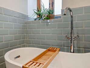 Ein Badezimmer mit einer weißen Badewanne, einem Holztablett und einem modernen Wasserhahn.