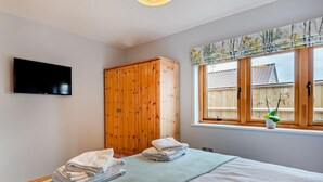 A bedroom with a bed, a wooden wardrobe, a TV mounted on the wall, and a window with a view of the outside. - 2 Bed in Axbridge (oc-91358) (Compton Bishop)