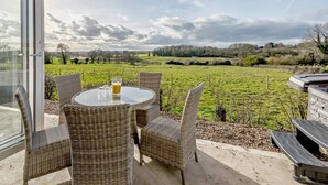 Un patio con muebles de mimbre, una mesa de vidrio y vista a un campo verde.
