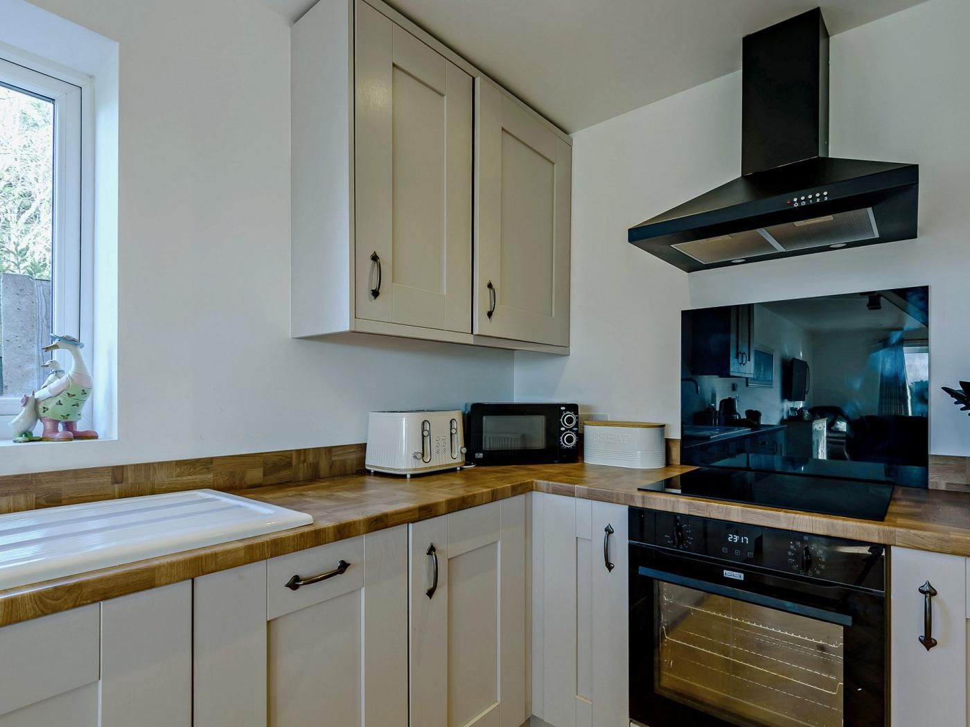 A modern kitchen with white cabinetry, a black range hood, a microwave, a toaster, and an oven.