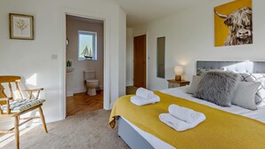 Un dormitorio con cama, una silla, una mesita de noche con lámpara, un cuadro y una ventana decorada con motivos de velero.