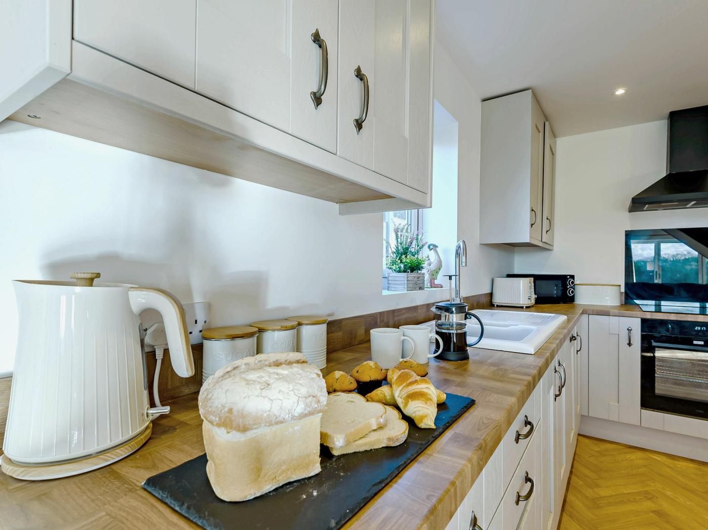 A modern kitchen with white cabinetry, a coffee maker, a bread loaf, and croissants on the counter.