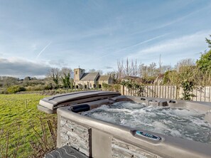 Ein Whirlpool mit Bedienfeld, umgeben von einer Rasenfläche, mit einer Kirche im Hintergrund.