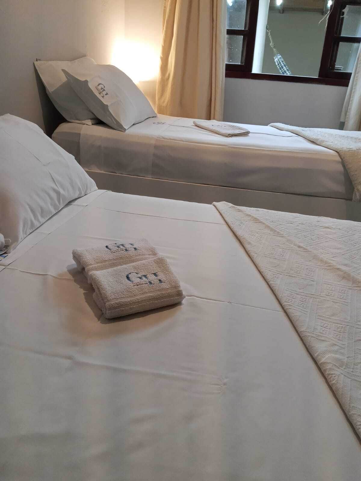 A hotel room with two beds, each with a pillow and a blanket. There are towels on the bed.