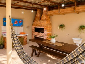 A rustic outdoor kitchen area with a brick oven, wooden table, and hammock.