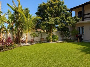 Un césped cuidado con una variedad de plantas tropicales y un edificio con techo de tejas.