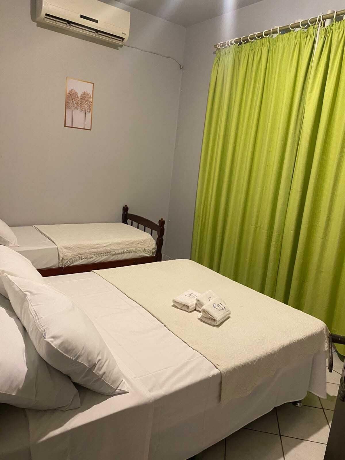 Quarto com duas camas, cortina verde e ar condicionado.