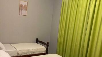 Quarto com duas camas, cortina verde e ar condicionado.