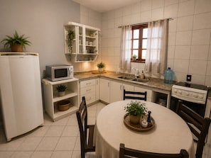A compact kitchen with a refrigerator, microwave, sink, and stove. There is a dining table with chairs and a potted plant on it.