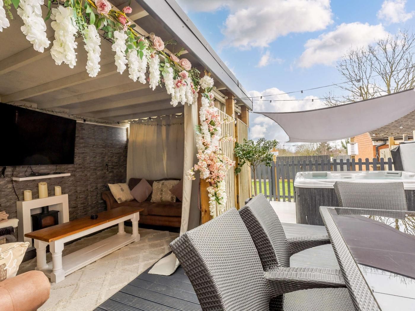 An outdoor patio with a stone wall, a flat-screen TV, a sofa, and wicker furniture.