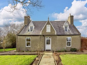 Une maison à deux étages avec une porte centrale, deux fenêtres à l’étage supérieur et une cheminée de chaque côté.