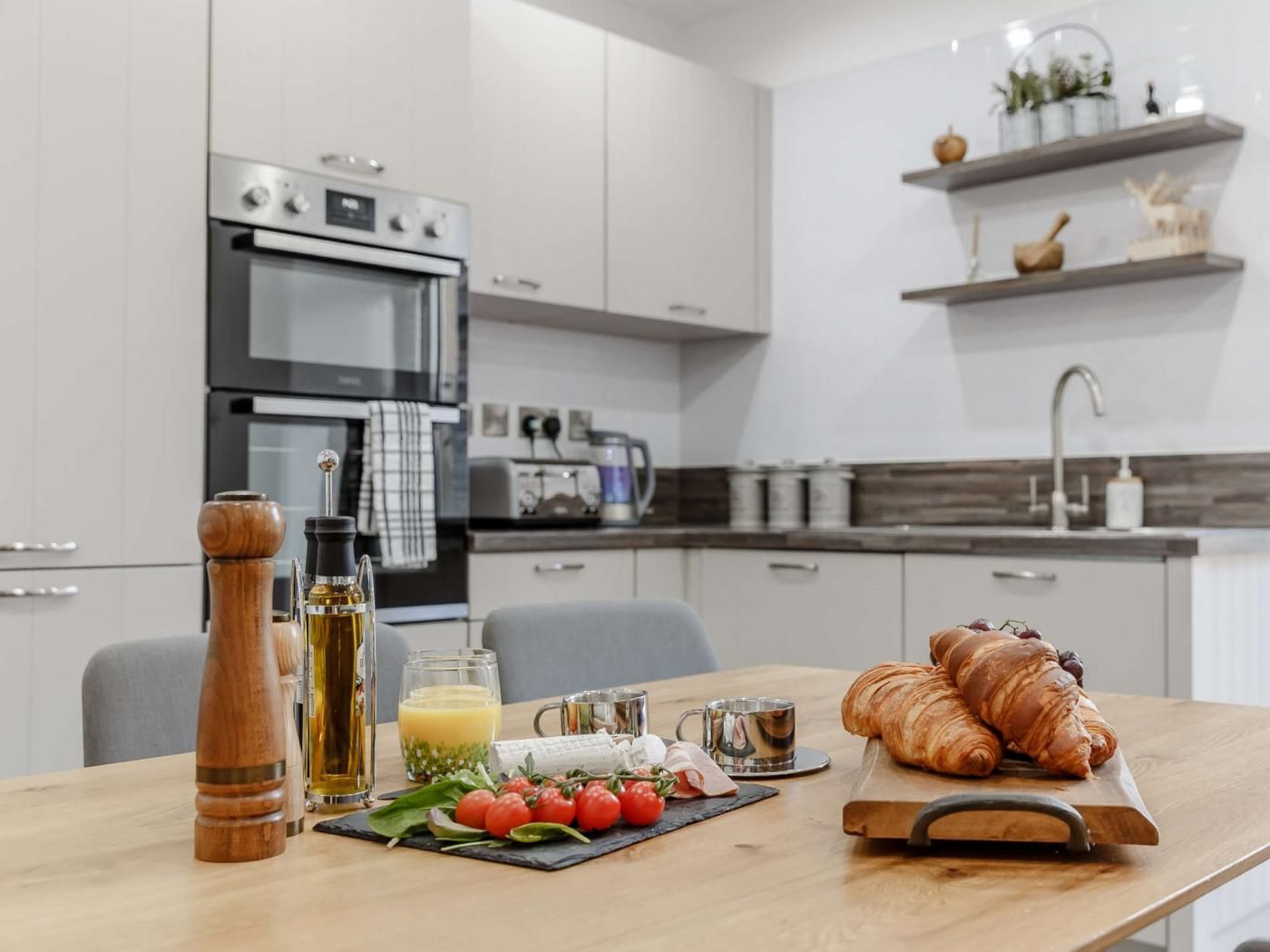 Een moderne keuken met een ontbijttafel, compleet met croissants, tomaten en een glas sinaasappelsap.
