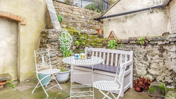 Eine Terrasse mit einem runden Tisch, zwei Stühlen, einer weißen Bank und einer Steinmauer.