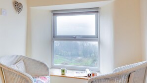 Ein Zimmer mit zwei Korbstühlen, einem Fenster mit Blick auf einen Wald und einem kleinen Tisch mit Tasse und Buch.