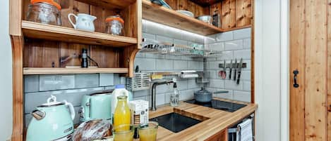 A kitchen with wooden shelves, a toaster, a kettle, and a sink.