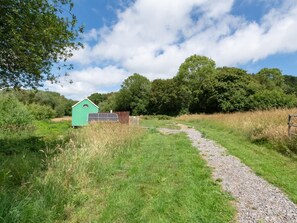 A rural path leading to a green building with a window, surrounded by grass and trees. - 1 Bed in Brighton (oc-90450) (Poynings)