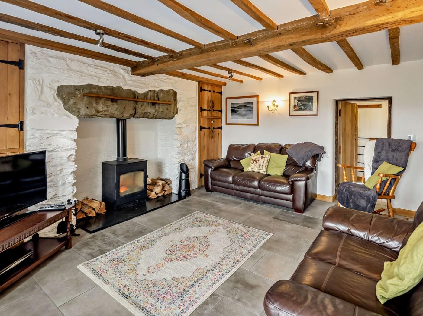 A cozy living room with a stone wall, a fireplace, a leather sofa, a wooden floor, and a television.