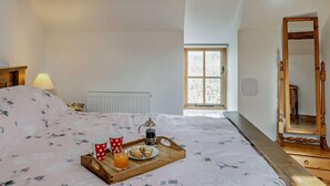 Ein Schlafzimmer mit einem Bett, einem Nachttisch mit Lampe, einem Fenster und einem Spiegel.