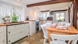 A kitchen with white cabinetry, a wooden dining table, and a clock on the wall. - 2 Bed in Exeter (oc-90455) (Tedburn Saint Mary)