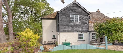 A two-story house with a stone roof, a small porch with chairs, and a fenced yard.