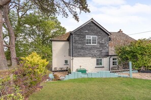 A two-story house with a stone roof, a small porch with chairs, and a fenced yard. - 2 Bed in Exeter (oc-90455) (Tedburn Saint Mary)