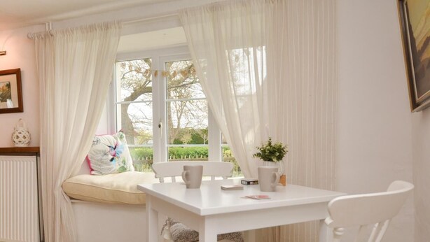 A room with a white table and chair, a window with curtains, a radiator, and a plant on the windowsill. - 2 Bed in Exeter (oc-90455) (Tedburn Saint Mary)
