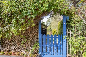 A blue gate with a picket fence, surrounded by greenery and a wooden structure. - 2 Bed in Exeter (oc-90455) (Tedburn Saint Mary)
