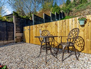 Eine Terrasse mit Holzzaun, Tisch und zwei Stühlen.