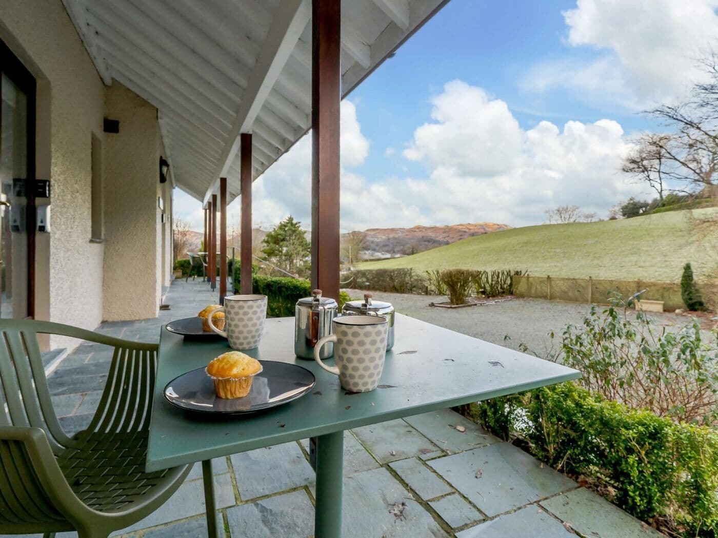 A covered outdoor seating area with a table, chairs, and a view of the countryside.