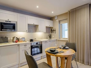 A modern kitchen with white cabinets, a microwave, an oven, and a dining area with a round table and chairs. - 1 Bed in Ambleside (oc-90636) (Ambleside)