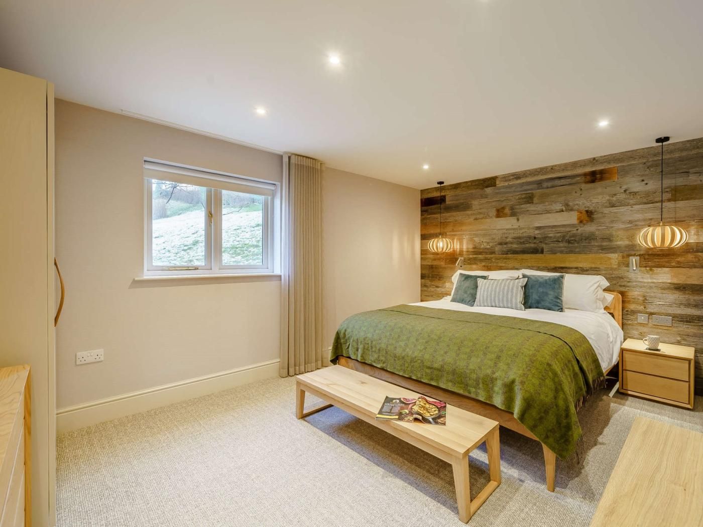 A bedroom with a bed, bedside table, bench, and a window.